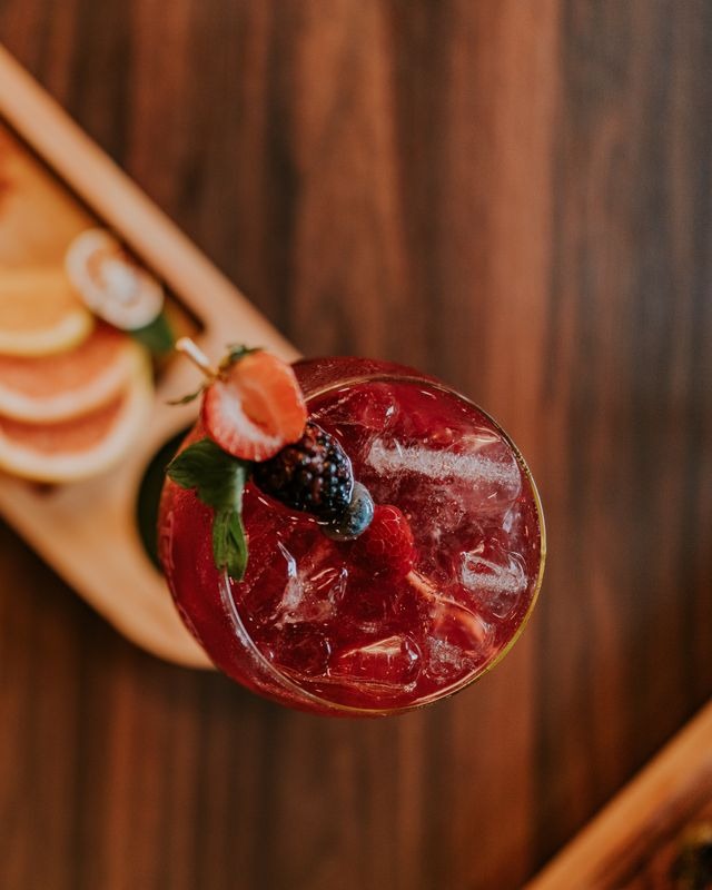 Overhead view of a raspberry cocktail with strawberry and blackberry garnish